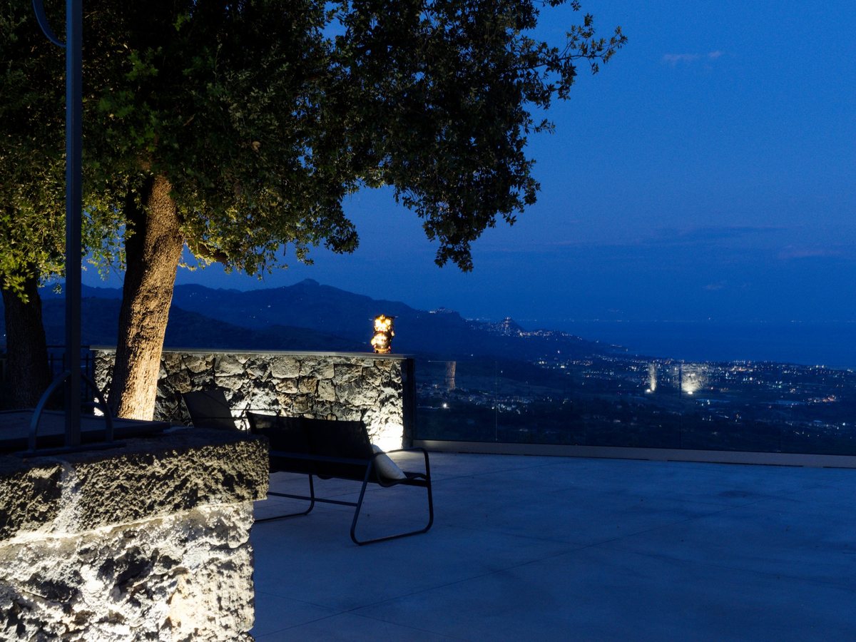 The illuminated terrace and olive tree overlooking the evening landscape